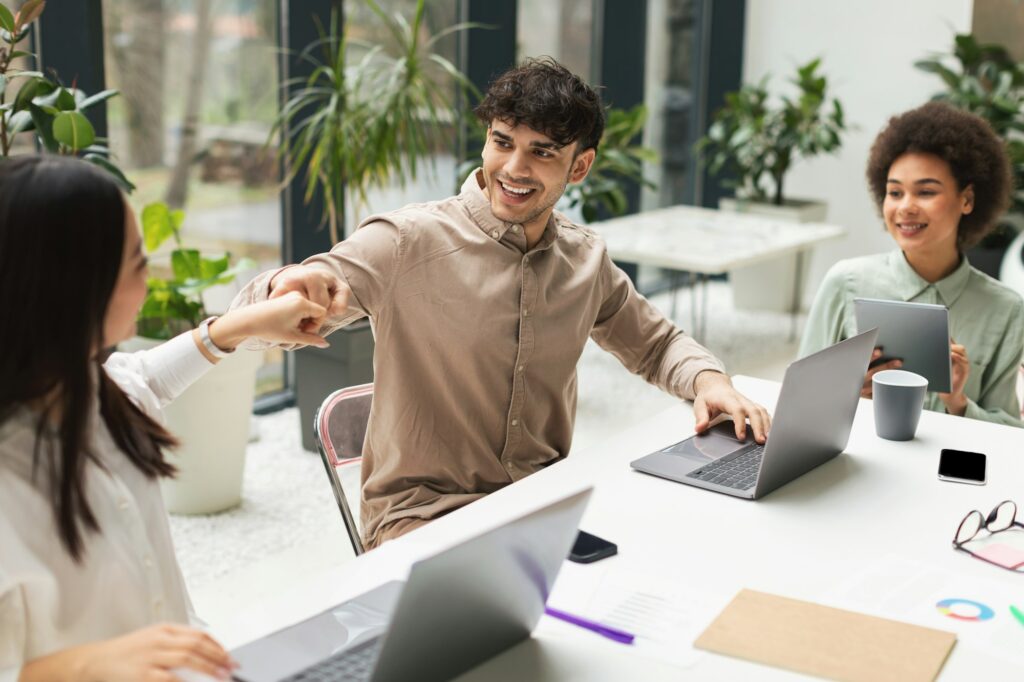 Happy Multiracial Colleagues Bumping Fists Celebrating Achievement In Modern Office